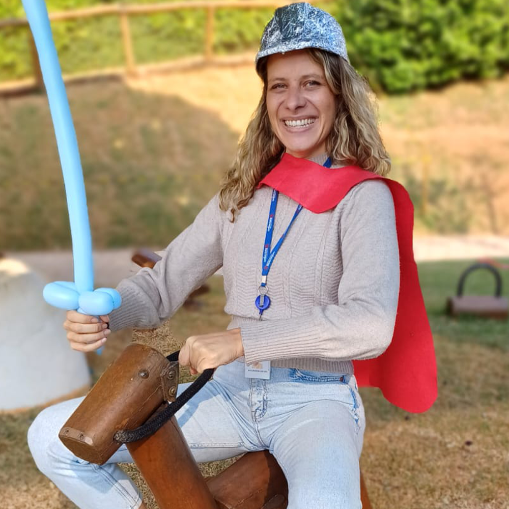 Alex montada em um cavalinho de madeira, com capa, capacete e espada de bexiga